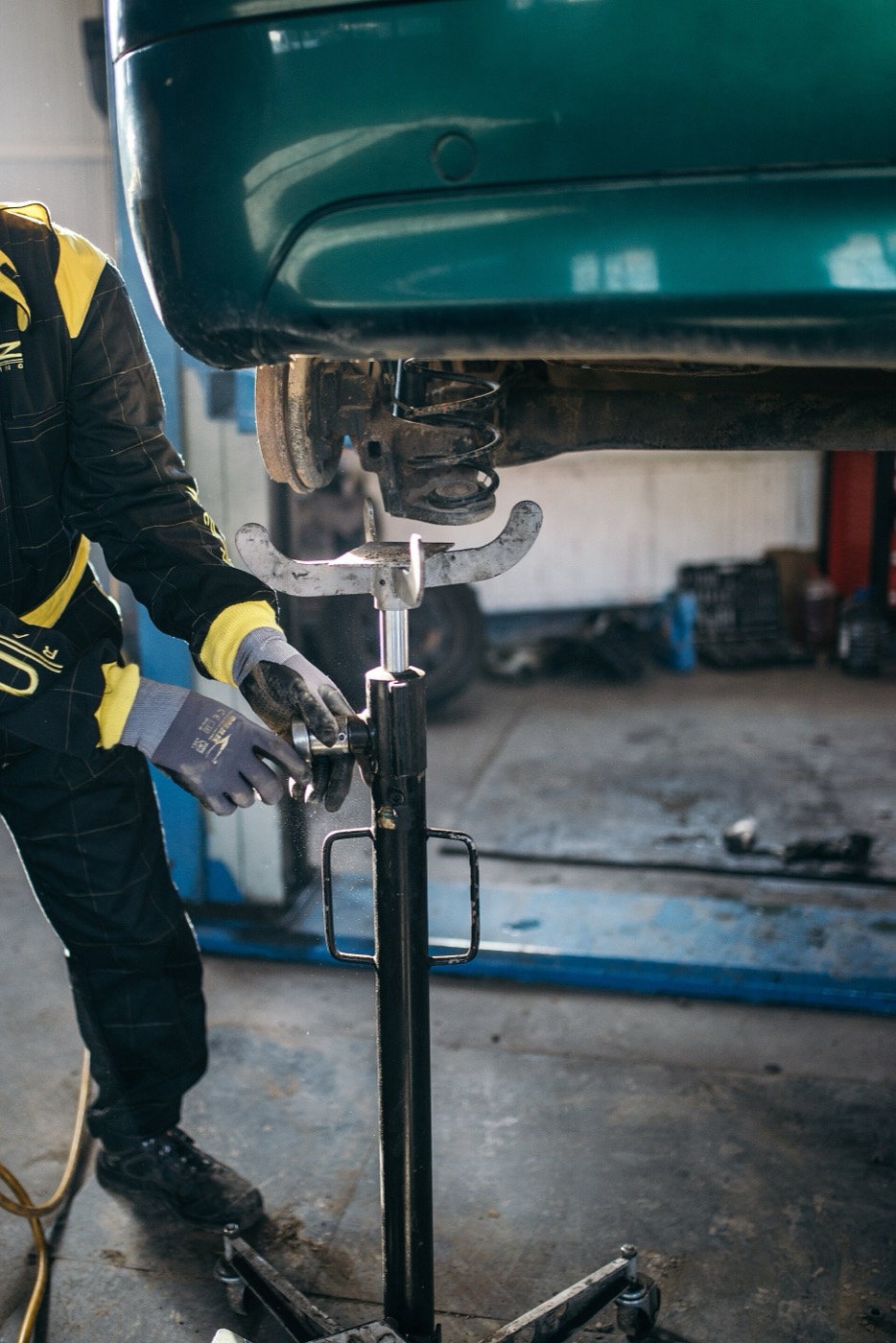 A mechanic in work gloves cranks a transmission jack under a lifted car